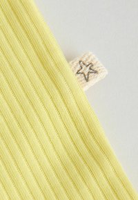 Material galben cu dungi, cu o etichetă mică bej care prezintă conturul unei stele negre pe un fundal deschis.