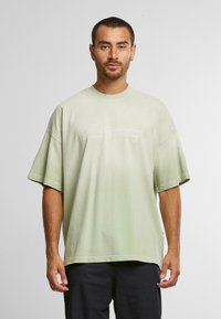 Lys grøn oversized t-shirt lavet af blødt stof, med korte ærmer og rund halsudskæring. Der er vist skriftsprog på forsiden.