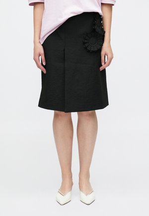 Svart knelangt skjørt med teksturert stoff, med tredimensjonale blomsterapplikasjoner på venstre side og et strukturert design.