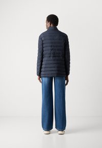 Jūras spēku pufīgais mētelis ar horizontālu quilted dizainu, augstu apkakli un garām piedurknēm, saskaņots ar platajām zilo džinsu biksēm un krēmīgiem apaviem.
