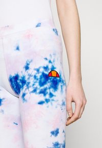 Vícebarevné tepláky s tie-dye vzorem v růžové a modré barvě. Na levém kapesním prostoru se nachází vyšívané logo slunce v oranžové a červené barvě.