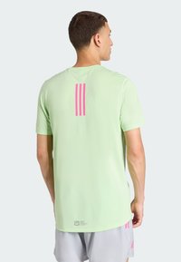 Camiseta de manga corta verde claro con un diseño de tres franjas rosas en la parte trasera, con una textura suave y escote redondo.