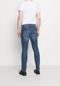 Slim-fit blå denimjeans med en lätt blekning, fem fickor, bälteshängare och kontrasterande sömmar. Kombineras med en enkel vit t-shirt.