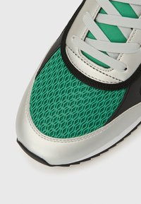 Zöld hálós sneaker ezüst díszítésekkel, hatszögletű mintákkal, fekete szegéllyel és szürke cipőfűzőkkel. Simított felület texturált részekkel.