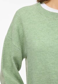 Gaiši zaļš adīts džemperis ar apaļu kakla izgriezumu, nolaistām pleciem un maigu tekstūru, kas raksturojas ar relaksētu piegriezumu visā garumā.