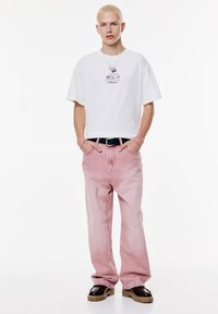 Witte graphic t-shirt met korte mouwen, gecombineerd met lichtroze baggy jeans. Zwarte riem, bruin platform schoenen en een zilveren ketting met hanger.