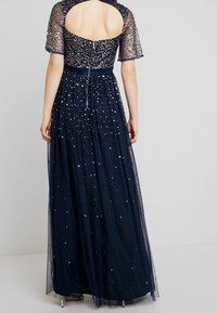 Námorně modrá róba s průhlednou korálkovou vrchní částí, krátkými rukávy a plnou tylovou sukní zdobenou rozptýlenými flitry. Design s otevřeným zadním dílem.