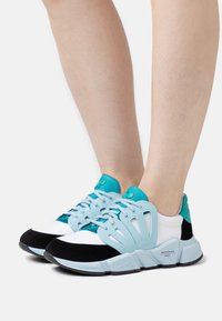 Le sneakers presentano una tomaia in rete leggera di colore bianco, arricchita con dettagli turchesi e neri. Un design unico della fascia laterale offre supporto.