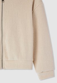 Giacca beige con zip, caratterizzata da un motivo testurizzato, con orlo e polsini a coste. Il materiale sembra morbido con una leggera lucentezza.