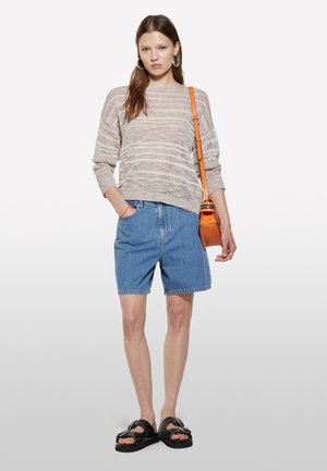 Maglione a righe beige chiaro, pantaloni shorts in denim blu, sandali platform neri e una borsa a tracolla arancione. Outfit casual con texture varie.