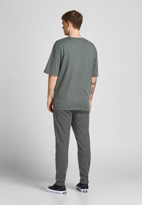 Graues, oversized T-Shirt mit kurzen Ärmeln, kombiniert mit dunkelgrauen Jogginghosen. Der Look wird mit lässigen Schuhen abgerundet. Einfache, weiche Stofftexturen.