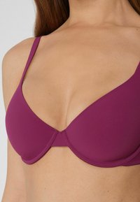 Soutien-gorge rembourré violet avec bretelles réglables, en tissu lisse et décolleté plongeant. Le design sans coutures présente des détails de couture minimes.