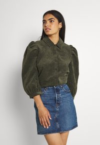 Mørkegrønn kordfløyelskjorte med knappestolpe, med puffermer. Kombinert med et blått denim miniskjørt.