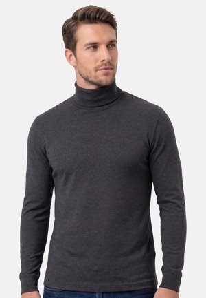 Mies, jolla on lyhyet ruskeat hiukset, pukeutunut tummaan harmaaseen pooloneuleeseen ja sinisiin farkkuihin, katsoo hieman oikealle.