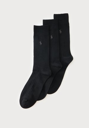 Trois paires de chaussettes noires côtelées montantes avec un petit logo brodé près du haut sur un fond clair.