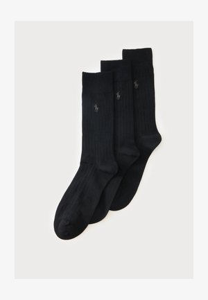 Trois paires de chaussettes noires côtelées montantes avec un petit logo brodé près du haut sur un fond clair.