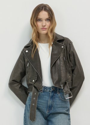 Cropped brown leather jacket with pointed lapels, zippered front, and silver hardware; paired with high-waisted blue denim jeans.