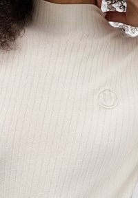 Sweter z prążkowanego dzianiny w kolorze ecru, z wysokim kołnierzem i subtelnie haftowanym logo na piersi. Miękka faktura, dopasowany fason.