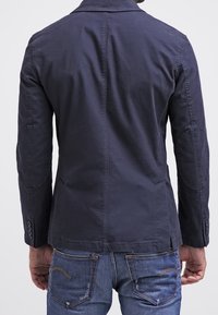 Mörkblå jacka med en figursydd design, skräddarsydd krage och armbågsfickor, tillsammans med ljusblå denimjeans.