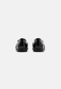Black leather shoes with a smooth finish, low profile, and subtle top stitching, featuring a closed toe and back, with slim rubber soles.