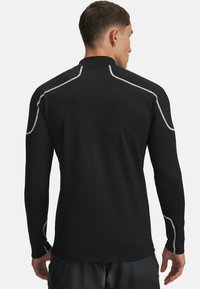 Sort langærmet skjorte med refleksiv sølvtråd langs skuldrene og ærmerne. Glat tekstur, tætsiddende design og høj krave.