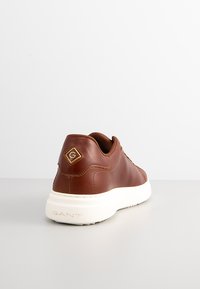 Braune Leder-Sneaker mit weißer Gummisohle, runder Form, genähten Akzenten und einem goldenen Logodetail an der Ferse.