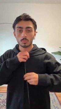 Sweatshirt preta com fecho éclair frontal e capuz, apresenta uma textura suave e bolsos laterais. A pessoa está a ajustar o fecho.