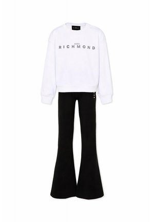 Sweatshirt blanc à manches longues avec le texte "John Richmond" associé à un pantalon noir évasé sur un fond uni.