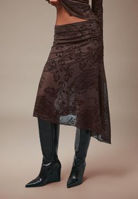 Smešani suknja s smeškom u smešnom uzorku, izrađena od lagane tkanine, koja ima visoki struk i asimetričnu donju ivicu, u kombinaciji s elegantnim crnim čizmama s oštrim vrhom.