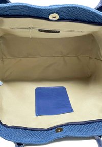 Modrá kabelka s texturovaným, plazím vzhledem. Interiér má béžovou podšívku a modrou kapsu na karty; viditelná je také kapsa na zip.