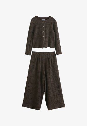 Tumepruun struktureeritud pika varrukaga nööpidega kardigan, mida kannavad sobivad laia säärega püksid, mõlemad krimpsutatud kangast.