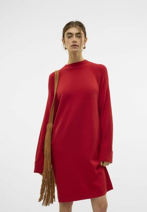 Röd överdimensionerad klänning med långa ärmar, ribbat detaljer vid axlarna och rundad halsringning. Kombinerad med en tan-färgad axelväska med fransar.