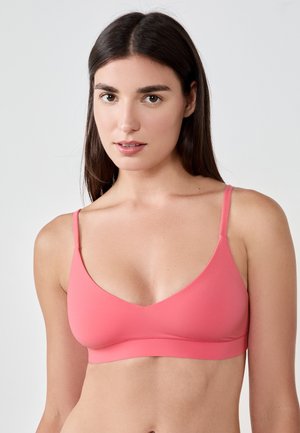Bralette wireless rosa con una texture liscia, spalline sottili regolabili e scollatura a specchio, caratterizzata da un design senza cuciture e hardware minimale.