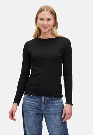 Haut noir à manches longues avec un col et un ourlet festonnés. Fabriqué à partir d'un tissu doux et extensible. Associé à un jean décontracté bleu clair.