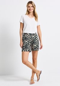 T-shirt blanc à manches courtes et décolleté en V associé à un short à motifs zèbres verts et ivoire, avec une coupe décontractée et des ourlets retroussés.