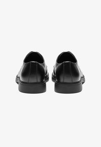 Black leather shoes with a smooth texture, rounded toe, low-profile sole, and minimal stitching detailing on the back.