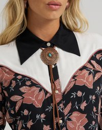 Svart blomstret bluse med hvit yoke, brun blomstermønster, kobberfarget bolo-navn med turkise detaljer og knappefester.