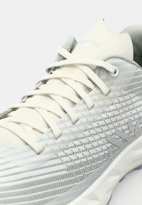 Grey athletic shoe with a breathable mesh upper, thin laces, and textured patterns, featuring a cushioned sole and minimal design elements.