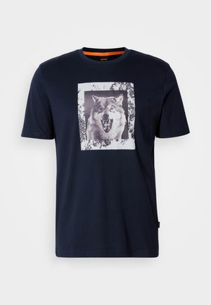 T-shirt in cotone blu navy con una grafica frontale di un lupo in bianco e nero, contornata da una cornice bianca texturizzata. Maniche corte e scollatura rotonda.