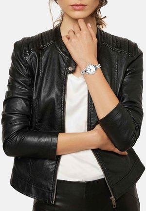 Sølvur med rund urskive, hvid skive og sorte timemarkører; kædet metallarmbånd. Sort læderjakke med ribbede skuldre.