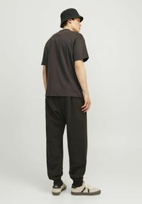 T-shirt nera di cotone a maniche corte, abbinata a pantaloni sportivi neri larghi e un cappello a secchiello nero. Sneakers in tonalità chiare con accenti a righe.