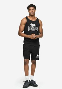 Czarny komplet z tank topem i szortami z białym logo "Lonsdale London". Koszulka z okrągłym dekoltem i luźnym krojem, do kompletu czarne sneakersy.