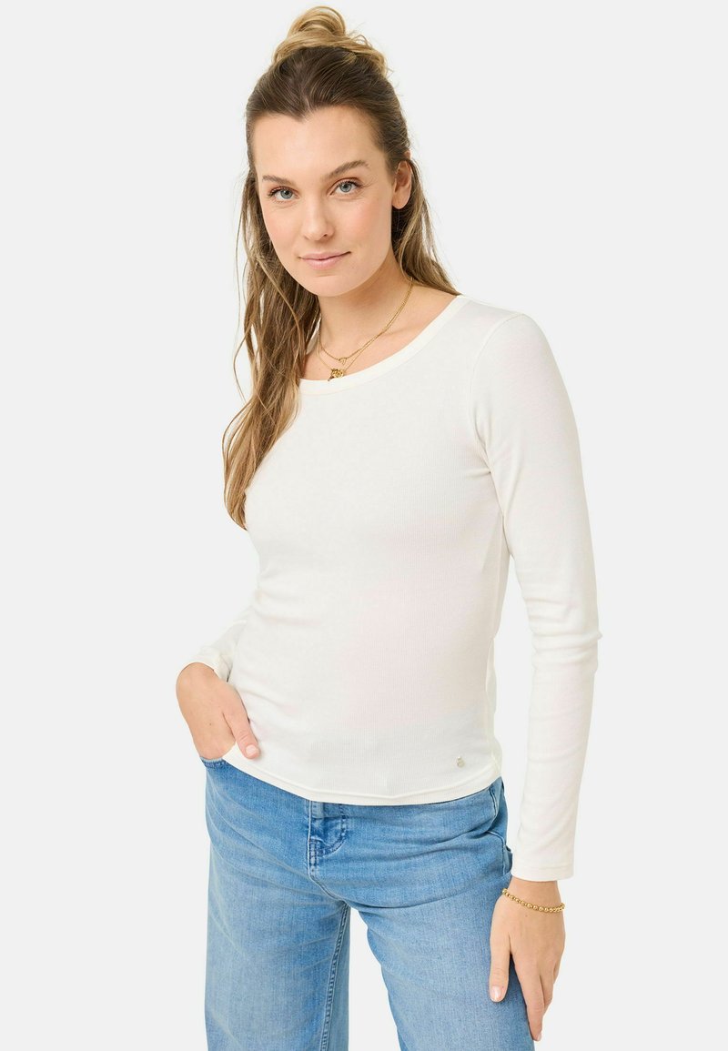 Top bianco a maniche lunghe con scollo tondo e dettagli laterali sottili, abbinato a jeans in denim blu chiaro. Vestibilità classica.