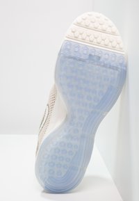 Semelle de chaussure avec un motif de semelle hexagonal translucide bleu et du caoutchouc texturé blanc près des orteils, inclinée contre une surface blanche.