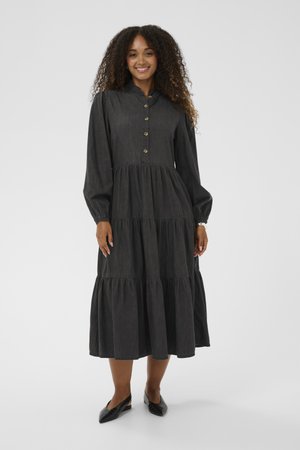 Rochie lungă neagră cu nasturi la față, cu straturi plisate și mâneci lungi. Fabricată dintr-un material moale cu o textură vaporoasă. Asortată cu balerini negri.