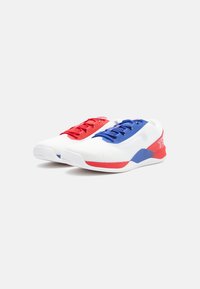 Sportieve schoenen met een witte mesh bovenkant en rode en blauwe accenten, voorzien van textuurveters en een gevoerde zool voor ondersteuning.