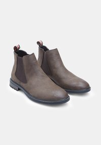 Botas Chelsea de cuero marrón con paneles laterales elásticos, puntera redondeada y suela de goma. Presenta una lengüeta con rayas rojas, blancas y negras.