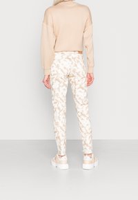 Sudadera beige combinada con pantalones blancos que presentan un sutil patrón abstracto en tono arena. El calzado es ligero, con una suela blanca gruesa y acentos transparentes.