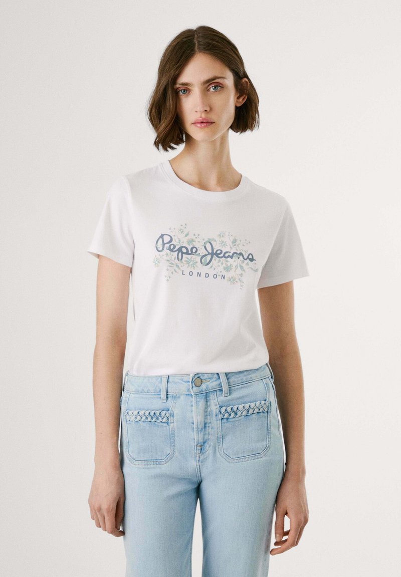 Vit bomullströja med "Pepe Jeans London"-logotyp och blommönster. Matchas med ljusblå jeans med flätade fickdetaljer.