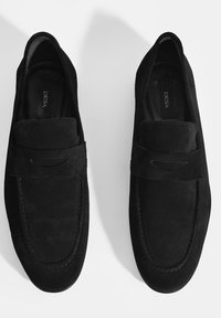 Schwarze Wildleder-Loafers zeichnen sich durch ein Mokassin-Design mit einer gestickten Spitze, einem einzelnen Riemen an der Vorderseite und einem glatten Innenfutter aus.